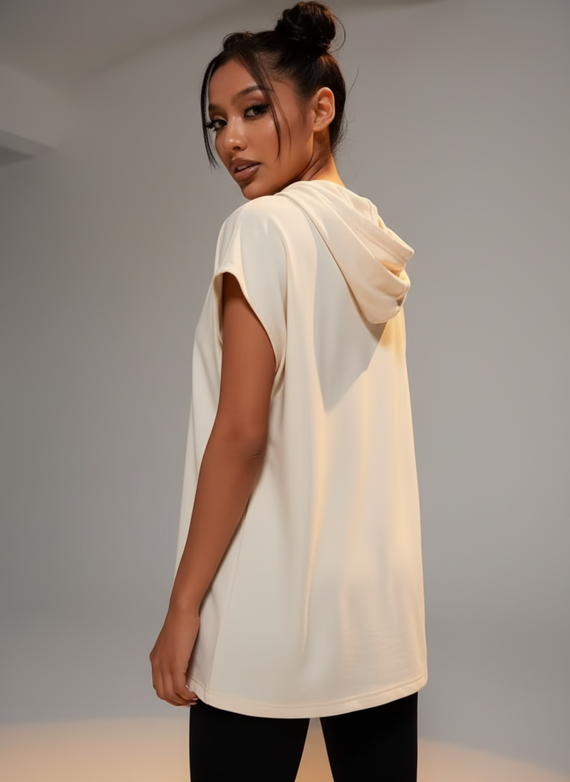 Woman in cream oversized short-sleeve sport hoodie, facing slightly away, against a minimalist neutral background.